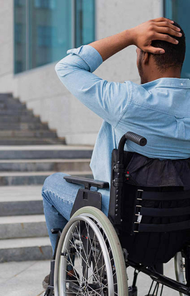 Ragazzo in sedia si trova in difficoltà di fronte a una scalinata senza rampa